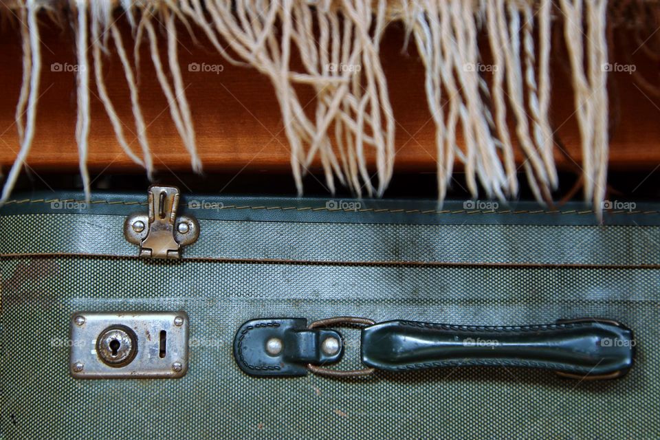 Close-up of an old green suitcase under a brown blanket