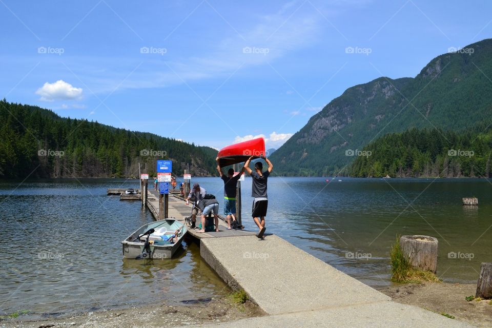 Red kayak adventure. Male youth carrying a red kayak on dock for lake trip