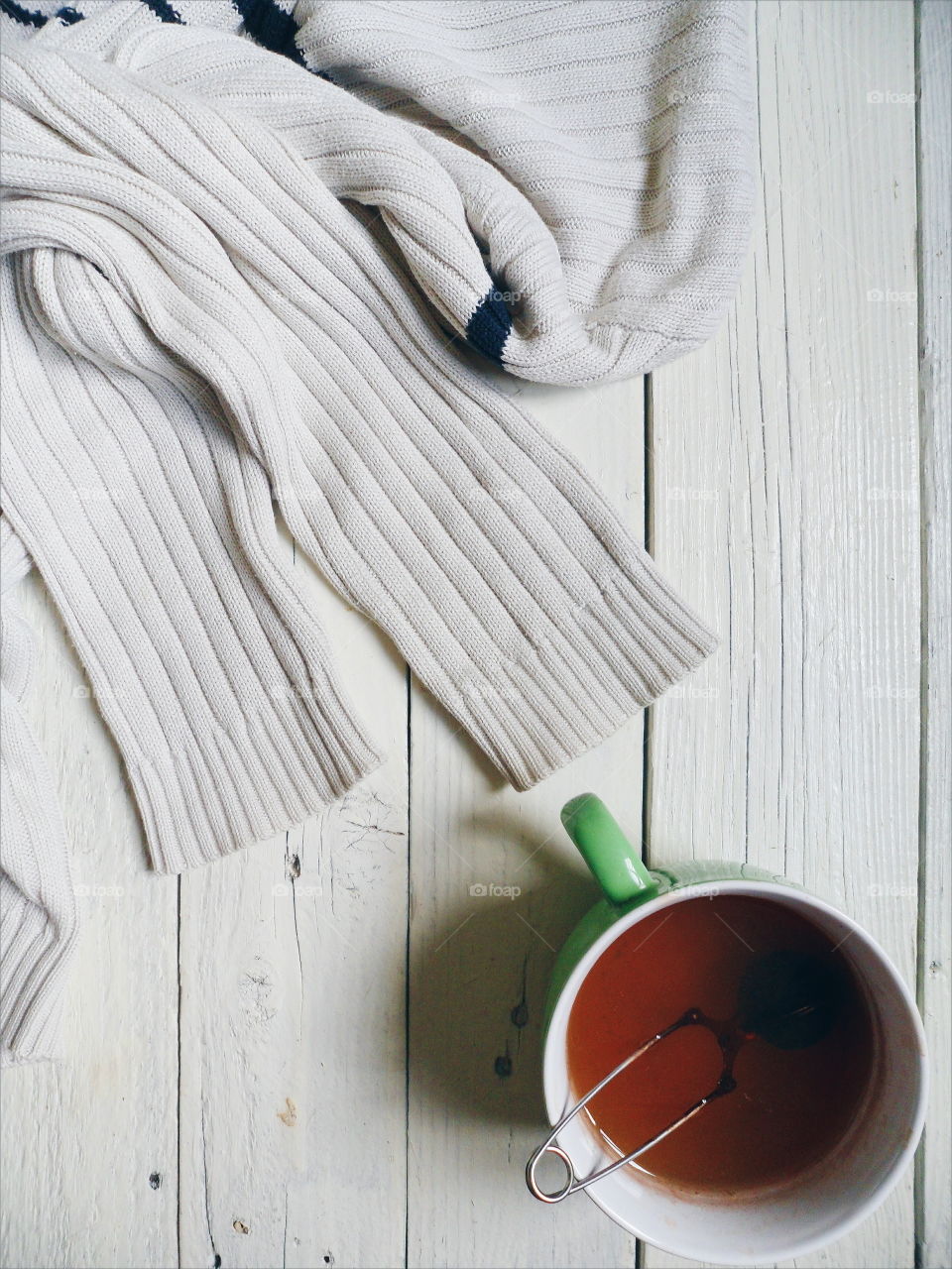 White sleeves of sweaters and a cup of black tea on white boards