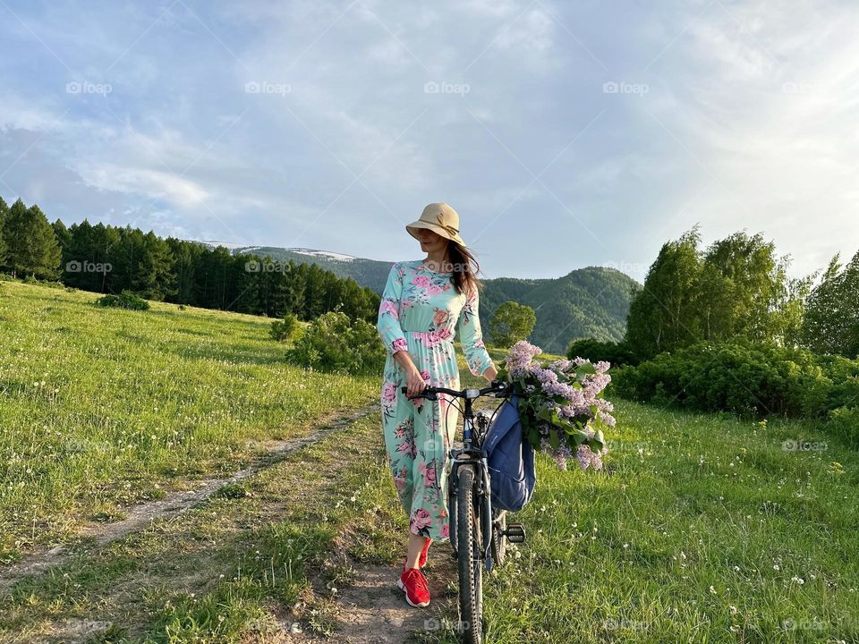 Girl in a dress with lilacs on a bicycle