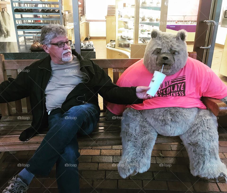 Retired man having a drink with a teddy bear 