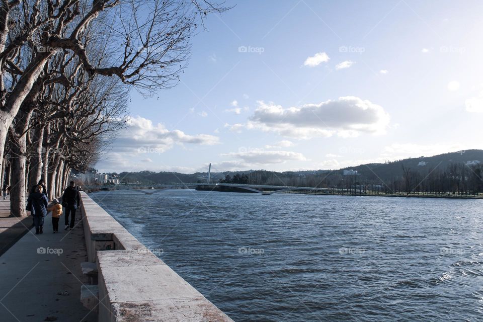 View over the river mondego in Coimbra, Portugal. Pedestrians bridge. People walking by the river.