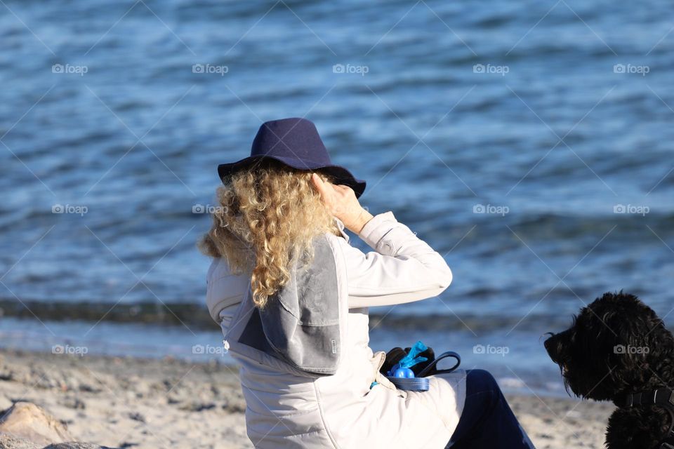 Woman sitting by the ocean, her hands going through her beautiful blond curly hair