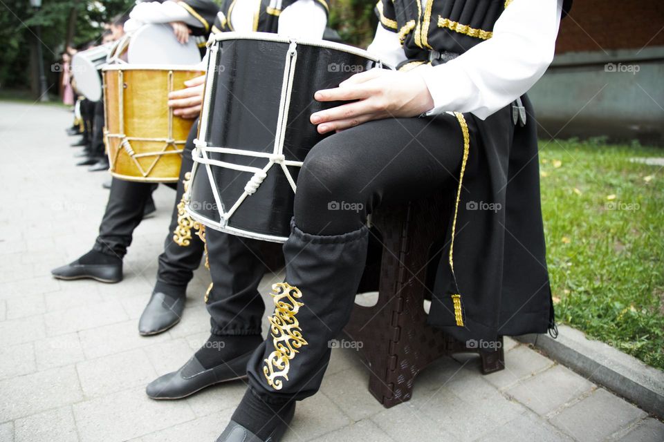 caucasian man in a ethnic costume sits on a chair and plays the drum . Drums of the peoples of the Caucasus.