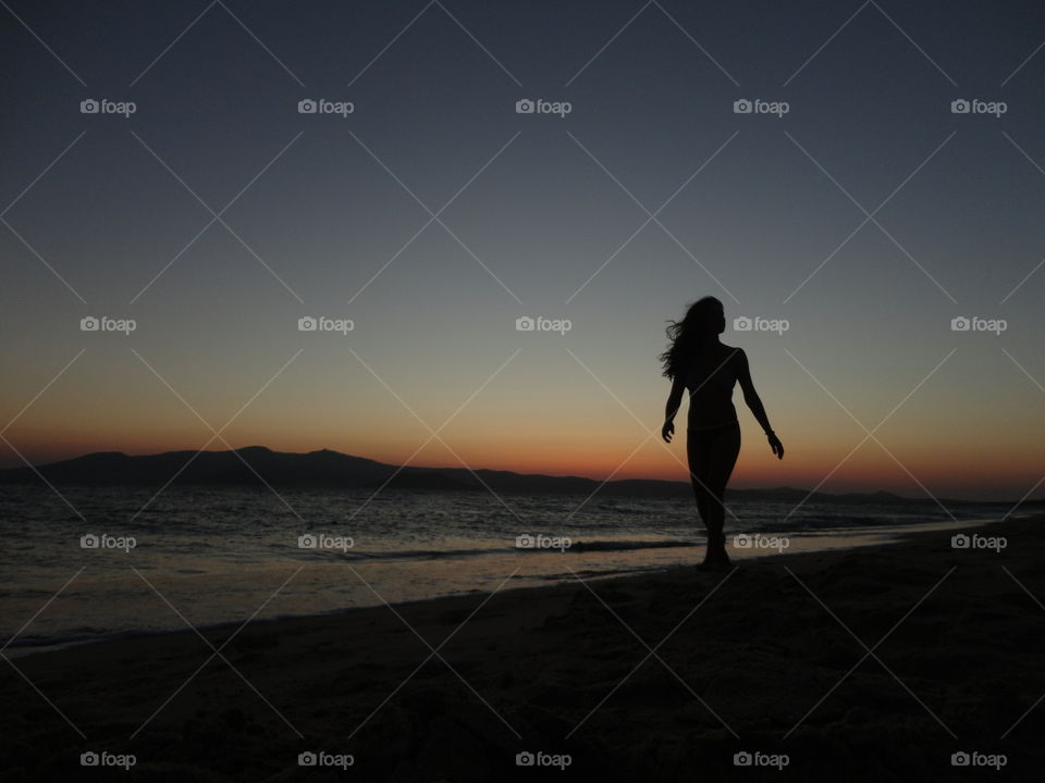 Silhouette of woman walking near the seashore at sunset