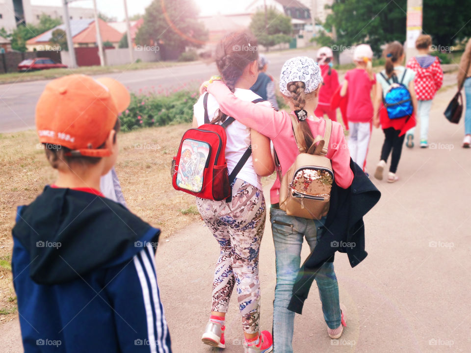 Young students with the backpacks walking together to the school in the warm autumn day 