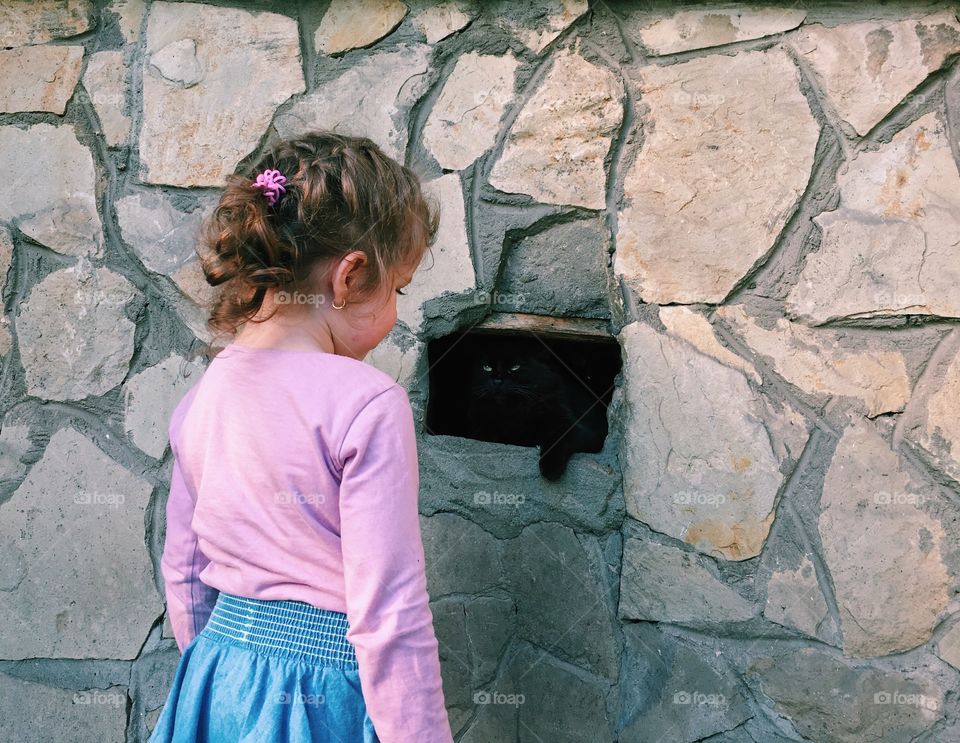 Little girl meeting cat hidden in the wall. 