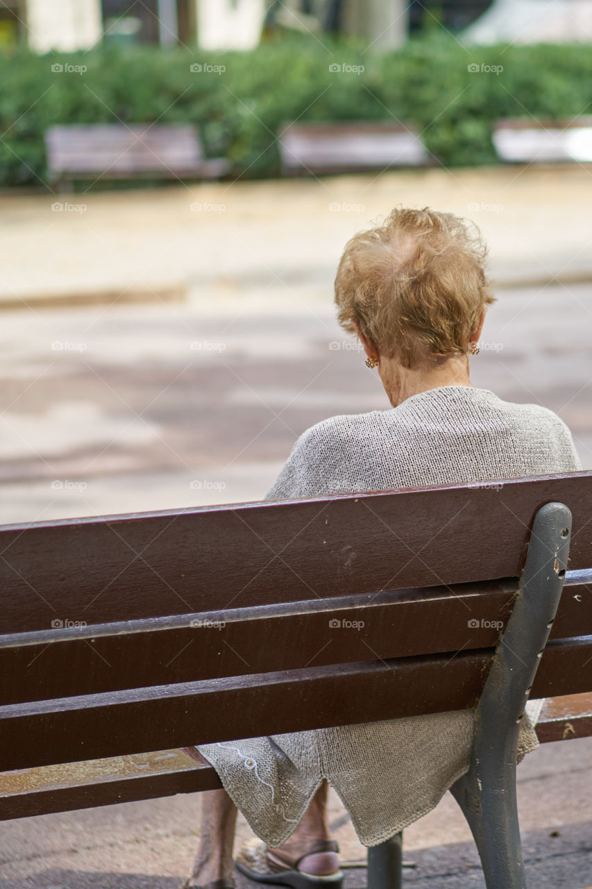 Elderly woman sitting in a street bench