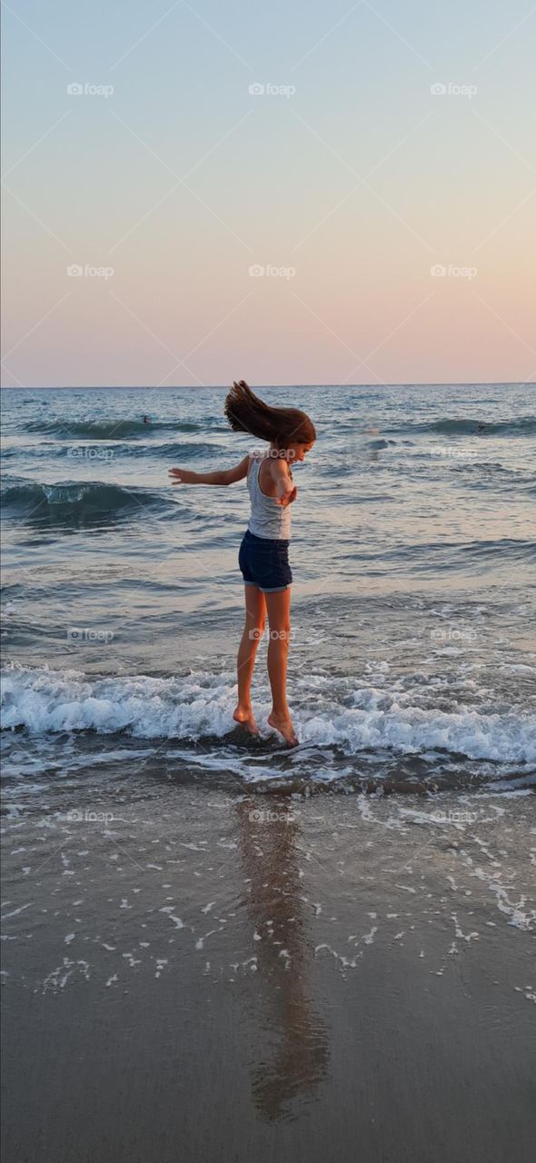 A girl in summer clothes jumps over the waves at sunset, her hair is flying