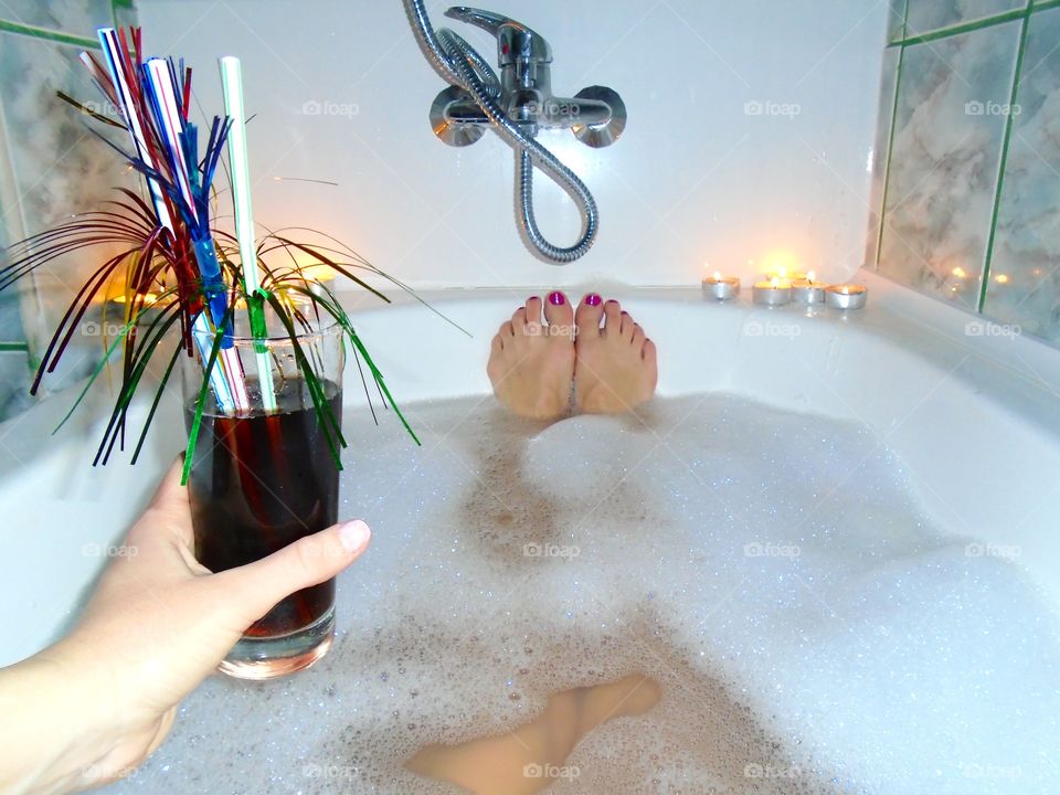 Woman's feet with red nail polish in bubble bath with candles and flowers