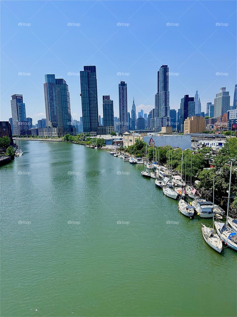 This gorgeous panorama presents itself overlooking “Newtown Creek” from the “Pulaski Bridge” that connects “Greenpoint”, Bklyn to LIC on a midsummer day. In the distance we see “Manhattan” incl. the “Empire State Bldg”. 2024. Hypnotic Productions