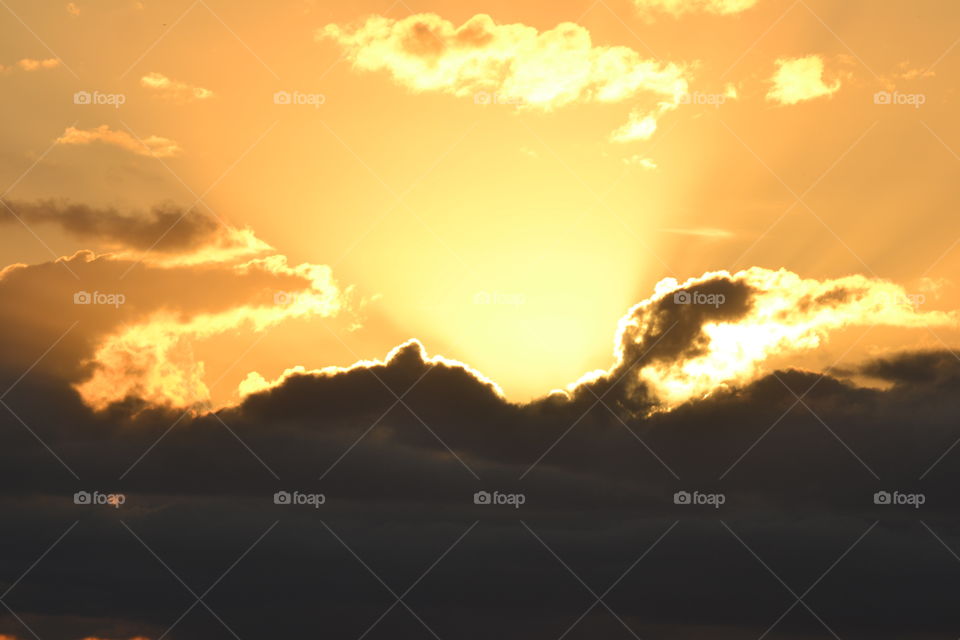 Golden sun rays reaching upward from a dark cloud against an orange sky at sunset