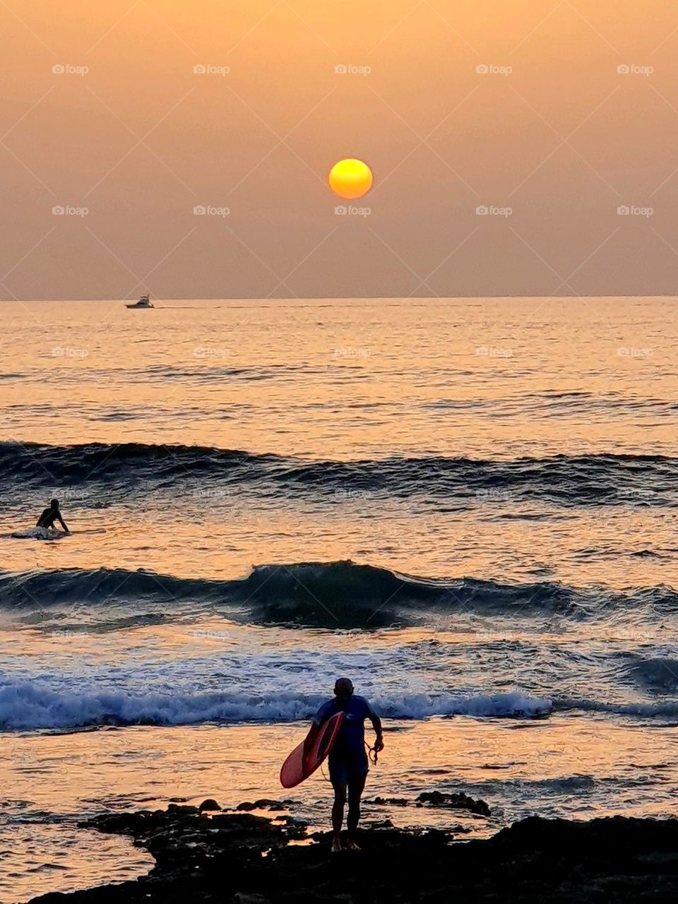 sunset at the beach- with an surfer at his way out of the ocean-