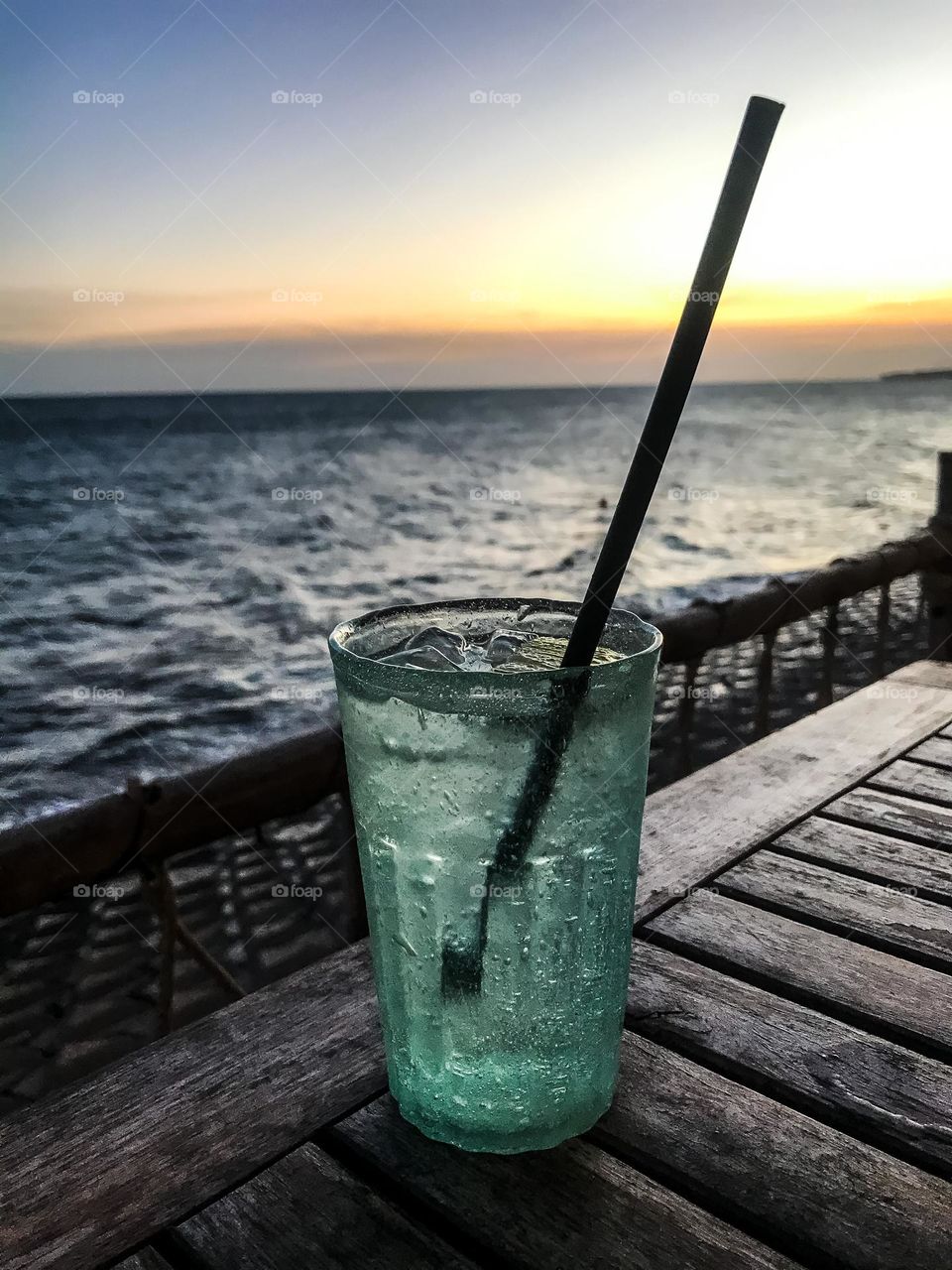 Cool glass of water on a wooden table at a seaside restaurant at sunset , sunset landscape 