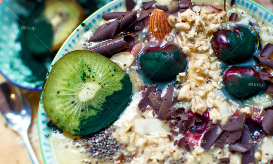 Decadent creative fruit smoothie bowl with healthy ingredients in abundance garnished with spirulina dipped cherries, kiwi, almonds, coconut, oatmeal, chia, and rich dark chocolate made from cocoa