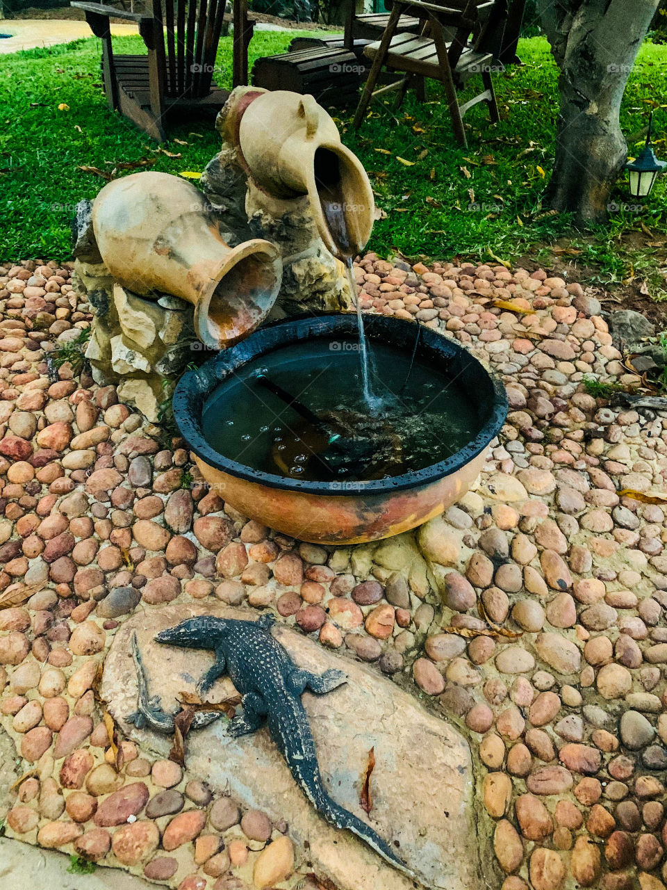 A ceramic sculpture of vessels pouring water into a basin, made of clay. With a stoney coarse background.