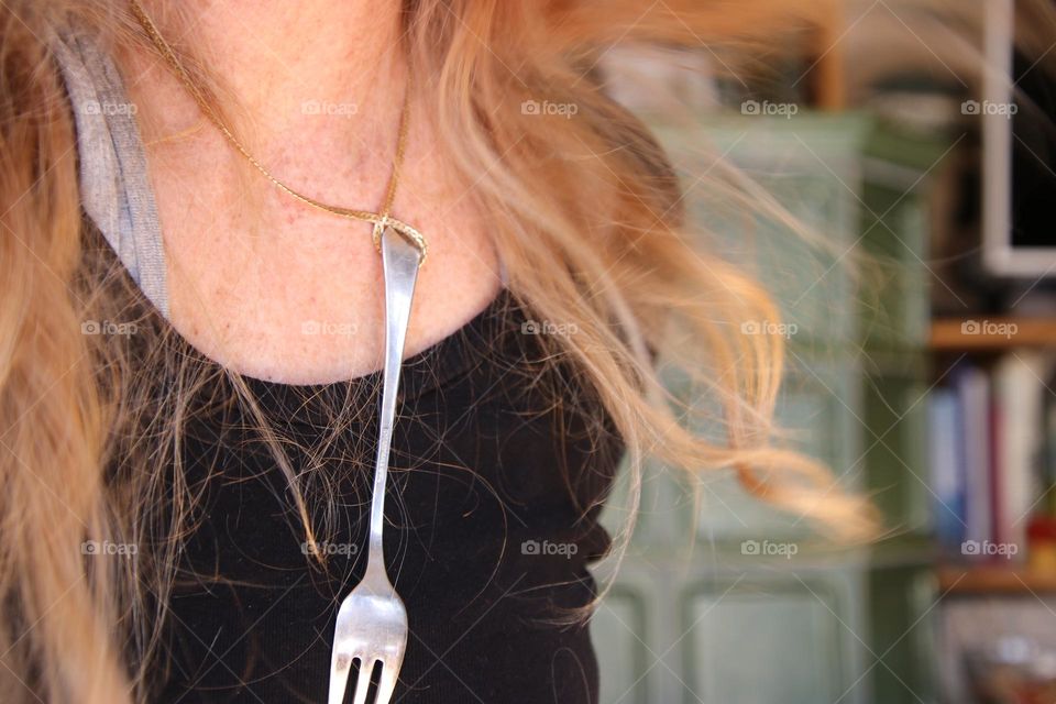 Close-up of a fork on a gold necklace on a woman with long hair