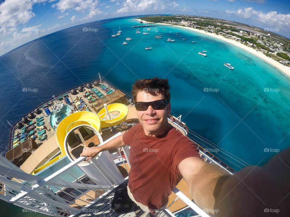 Man taking a selfie on top of a cruise ship in front of a Caribbean tropical island of grand Turk