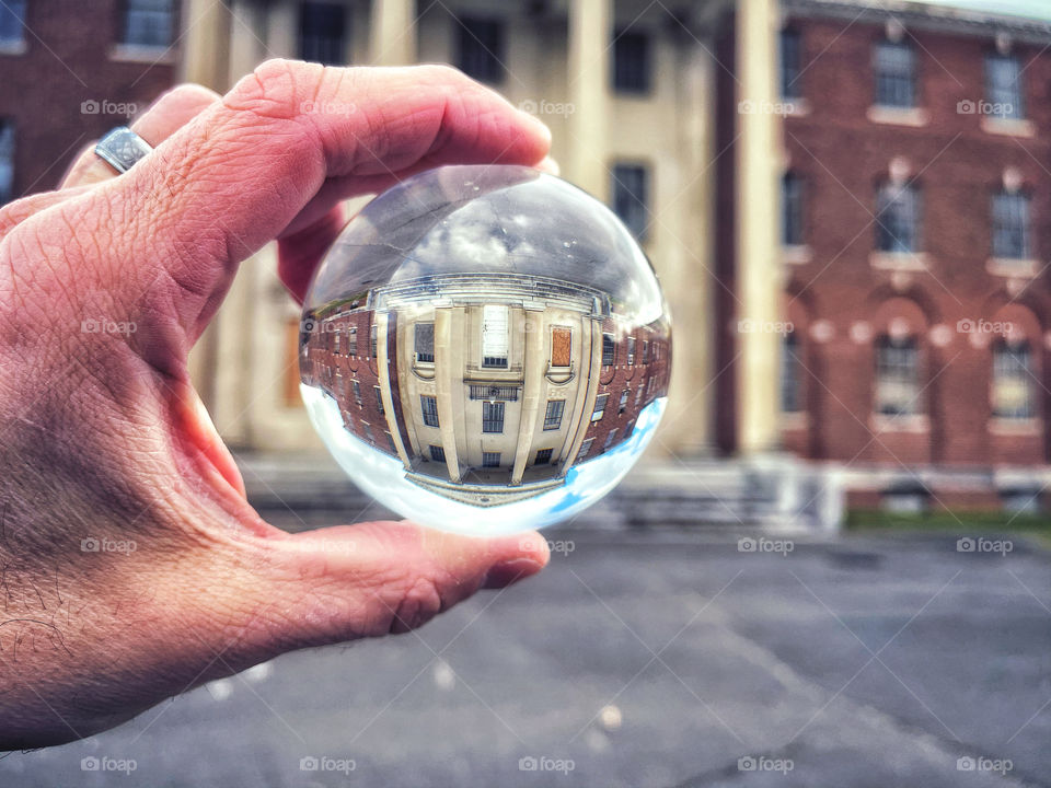 A mans hand holding a crystal ball in front of a derelict building 