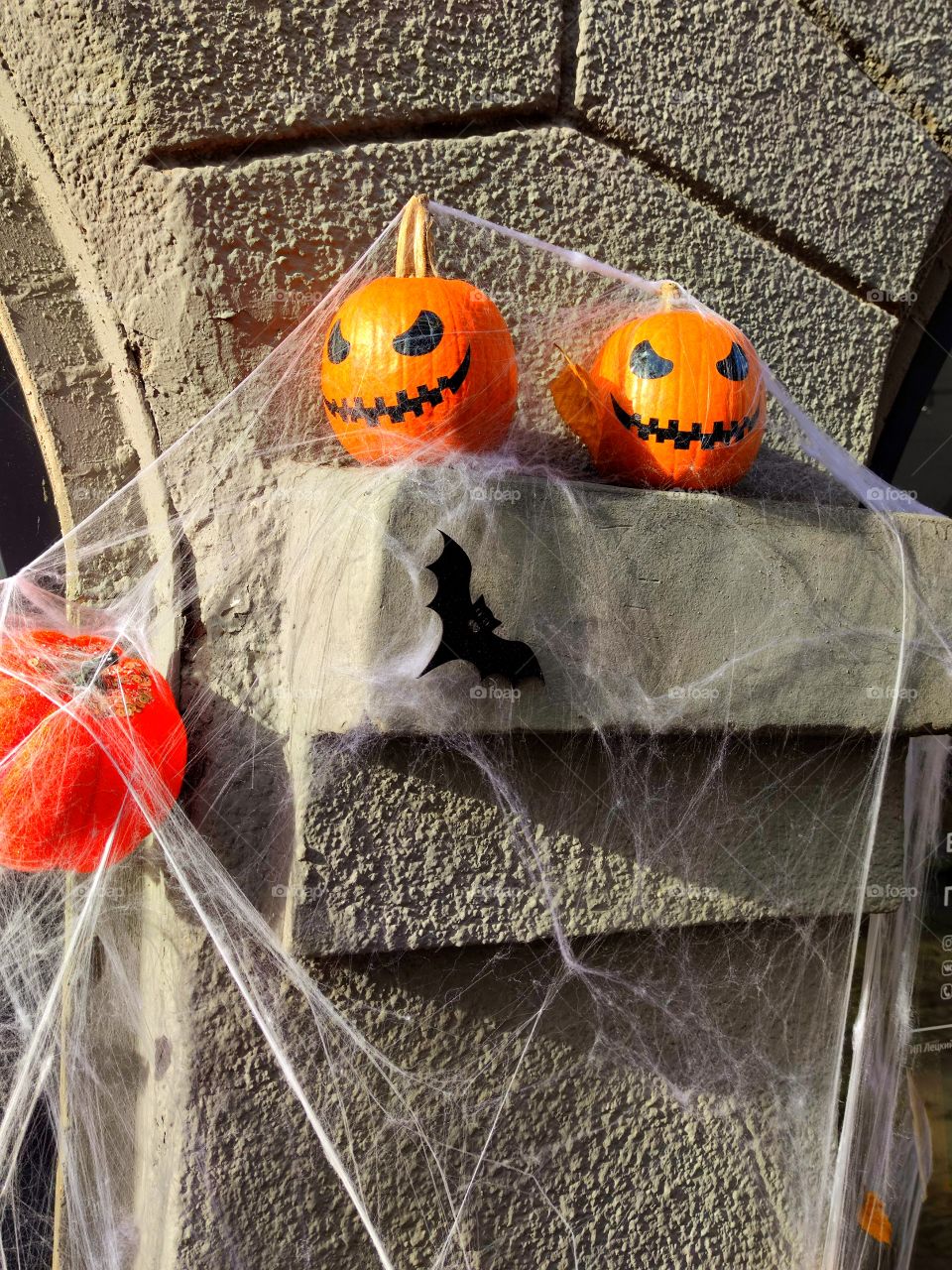 Halloween.  Two scary pumpkins lie on the parapet of a stone wall and are covered with cobwebs