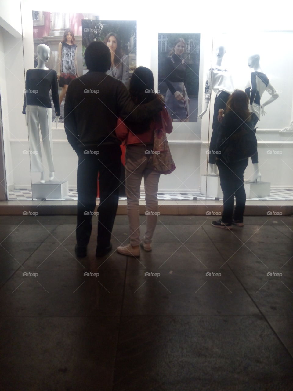 gente mirando un aparador de una tienda de ropa con modelos y maniquíes atrás del vidrio, vistiendo ropa de moda y temporada