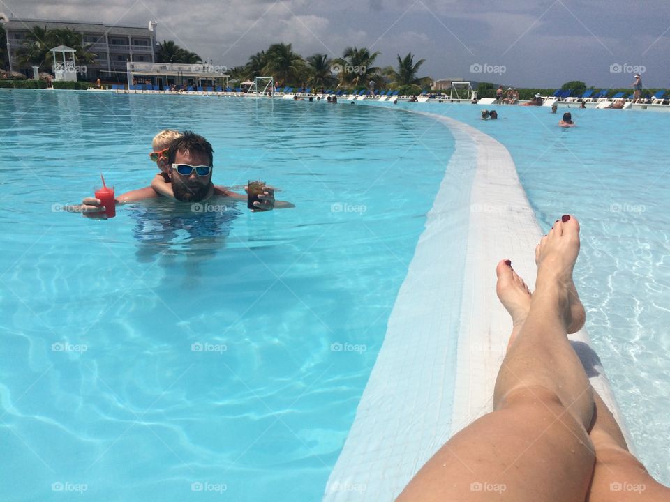 Man with child in infinity pool holding glass of juices in hand