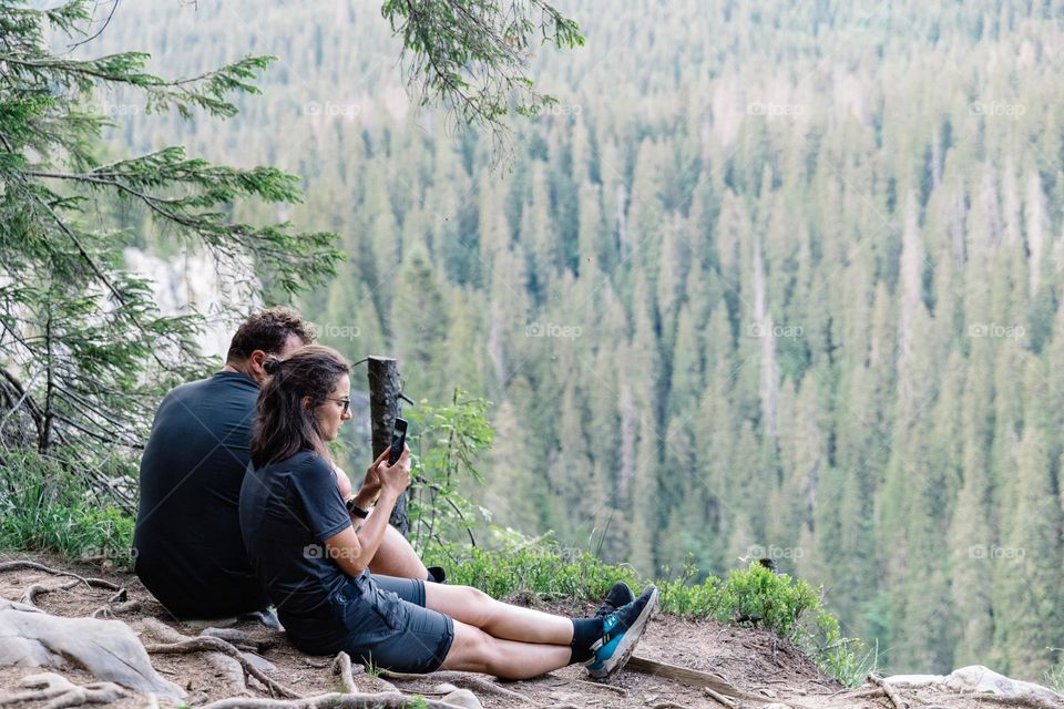 Young woman using her phone to take photos for social media, while doing a hike in the mountains.