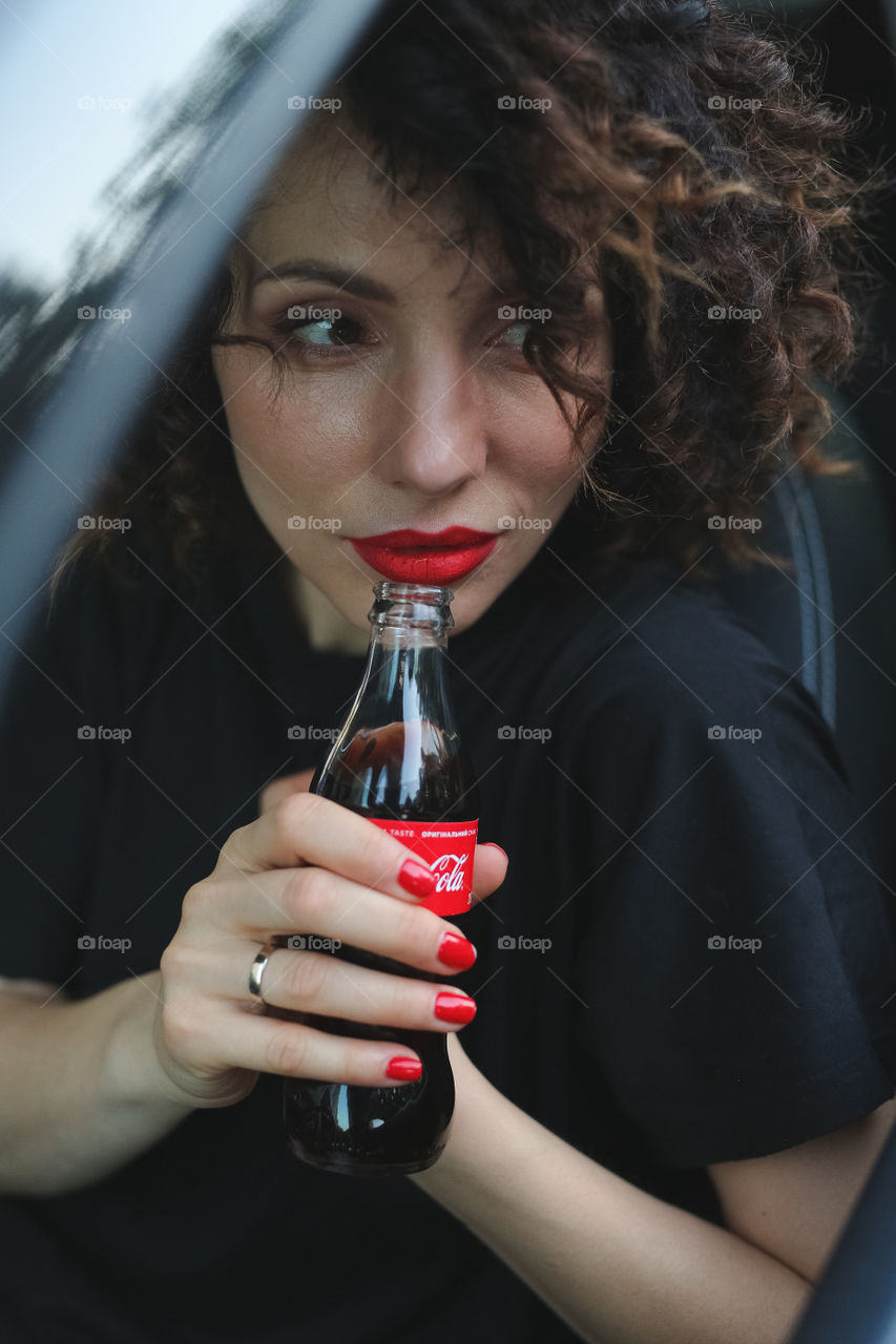 beautiful curly-haired brunette sitting in the car and drinking Coca-Cola, a delicious drink.  the girl is going to go to work