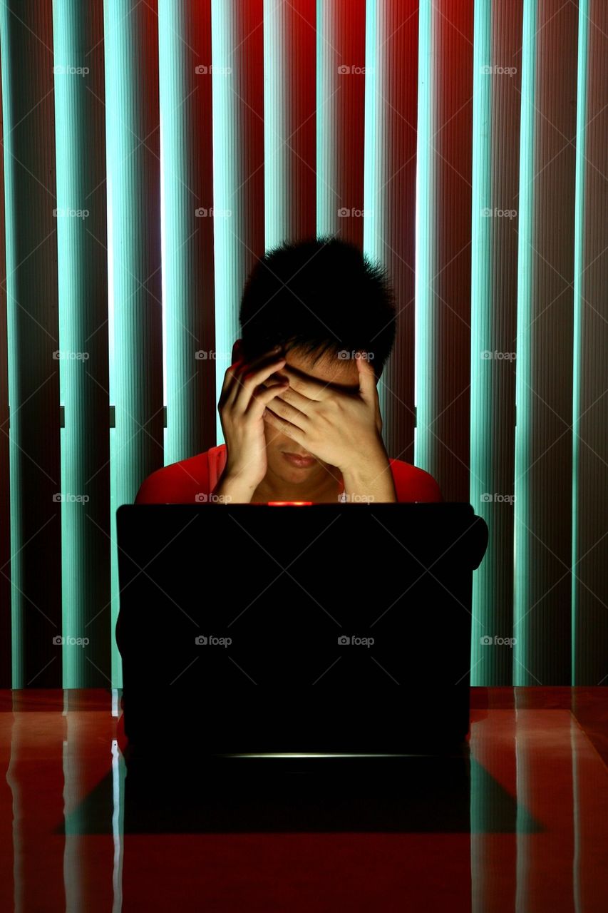 teenager in front of laptop computer covering his eyes