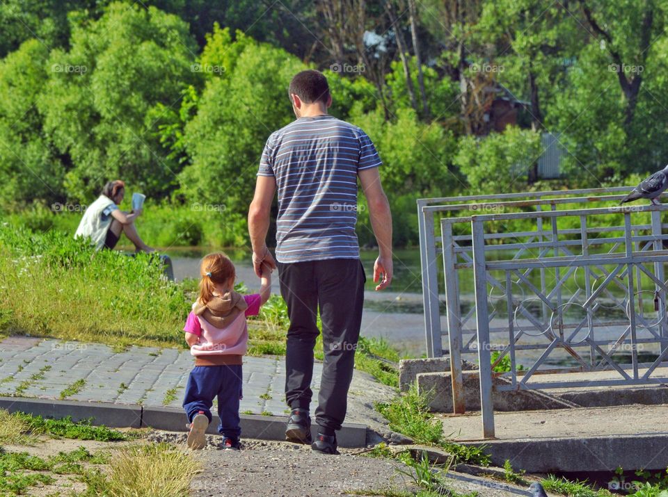 father walks along the embankment with his little daughter