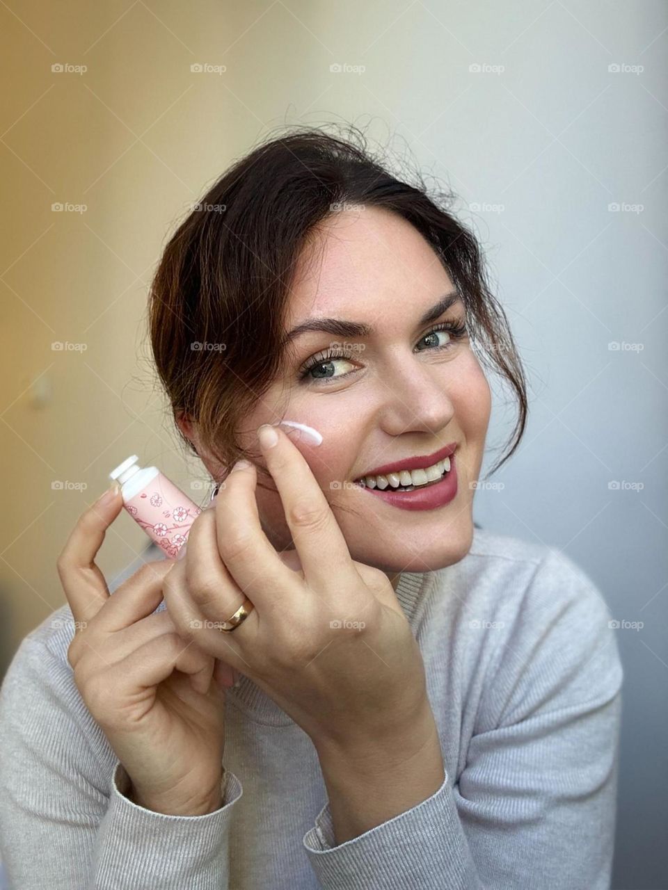 Woman’s portrait with product, girl holding a cream in her hands, creaming her face 