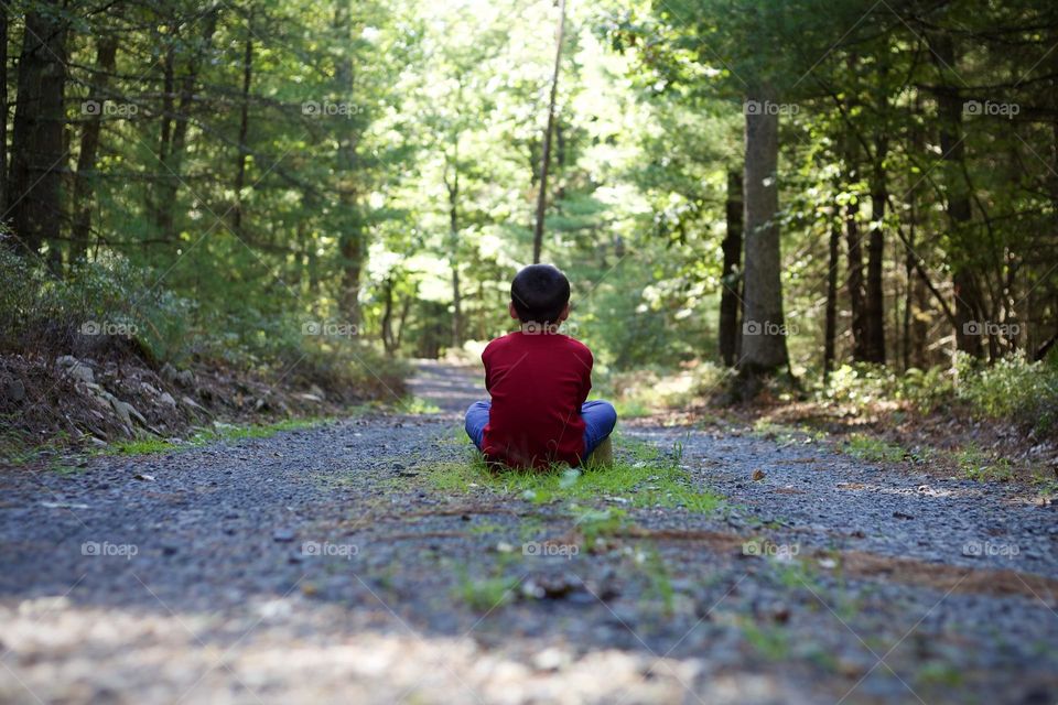 Red on the Trail; Young boy sitting on gravel road in the middle of the woods