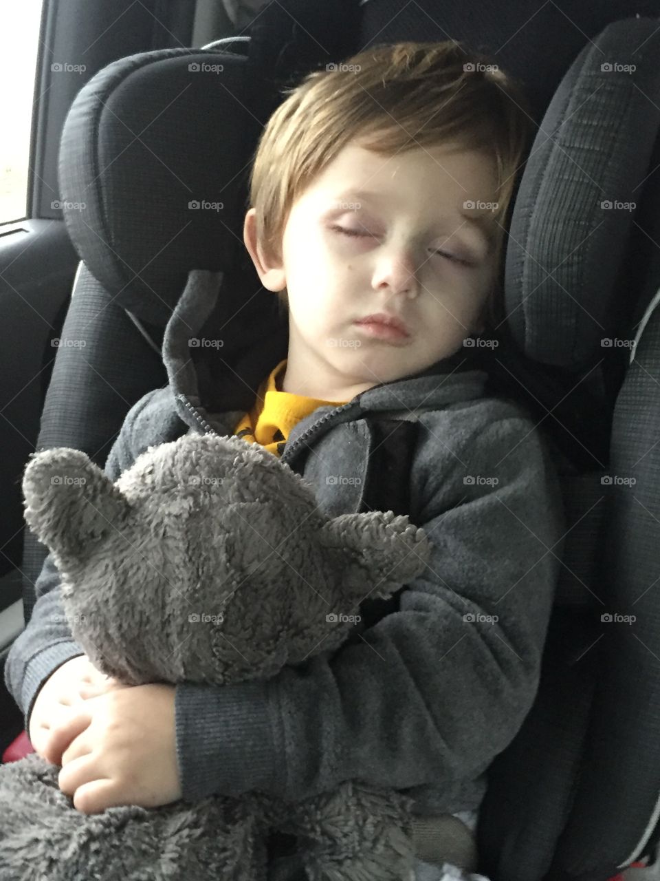 Boy sleeping in the car with teddy bear