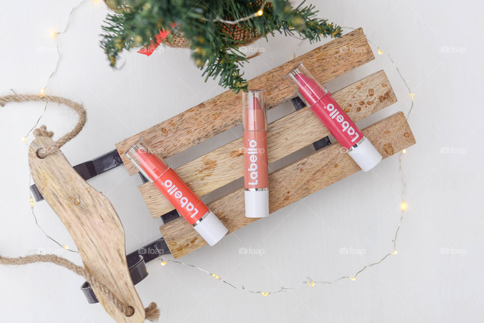 Row of Labello lip crayons on a mini wooden sled next to a small pine tree