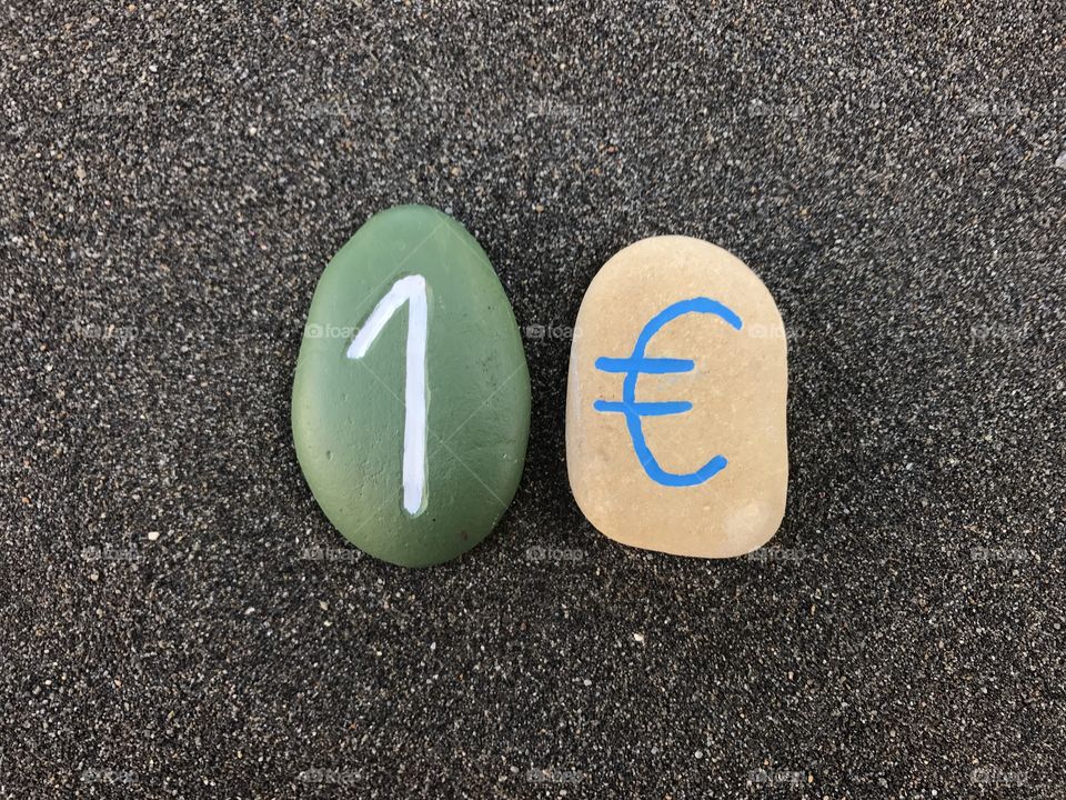 1 Euro with colored stones over black volcanic sand 