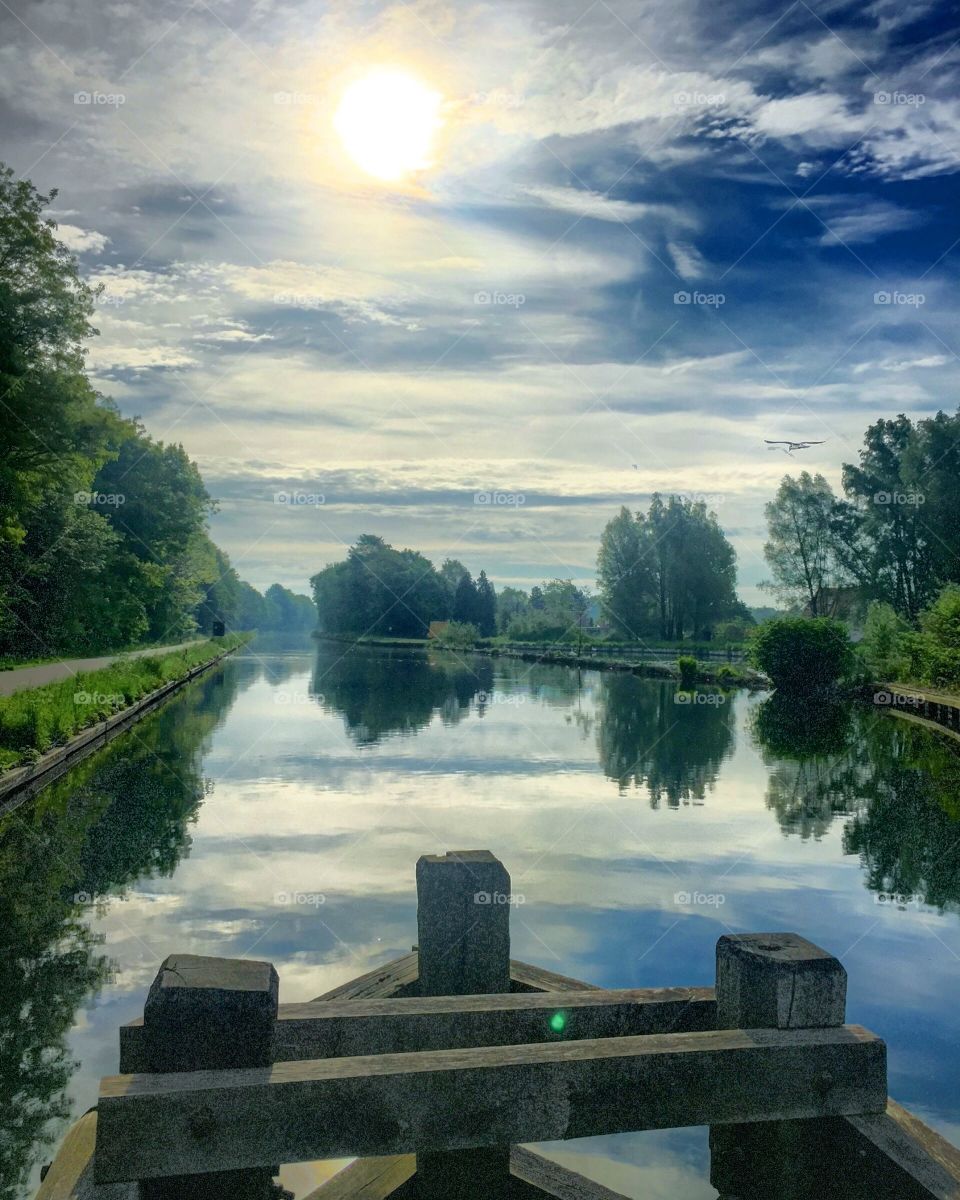 Painted looking Clouded and sunny sky reflected in the water of a river in a green rural Countryside landscape 