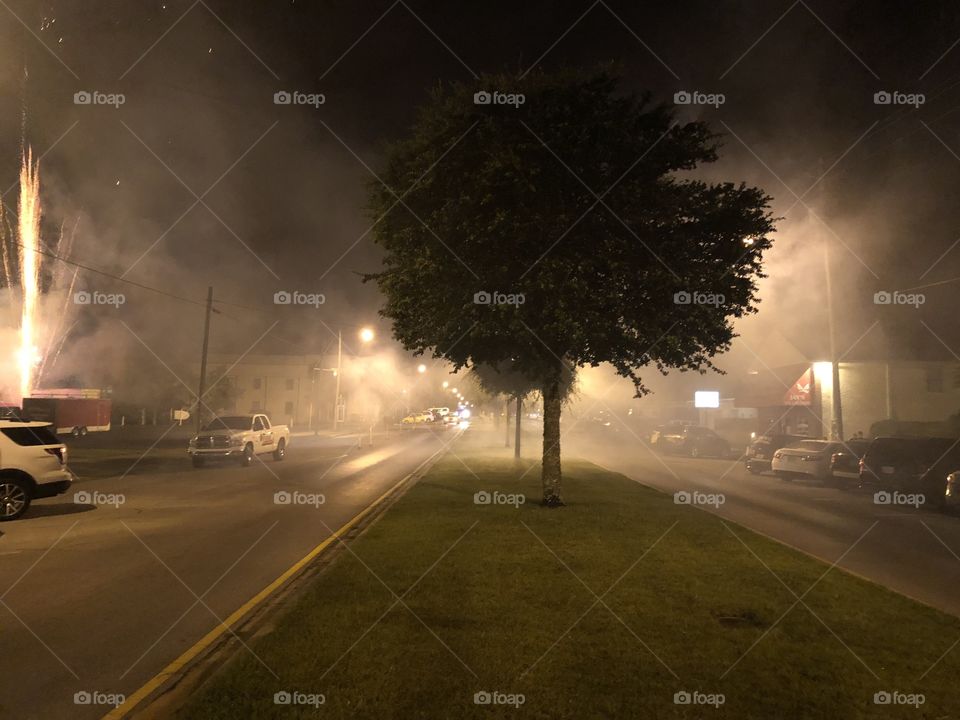 Tree in the middle of the street surrounded by smoke from fireworks I like the way the tree is backlit 
