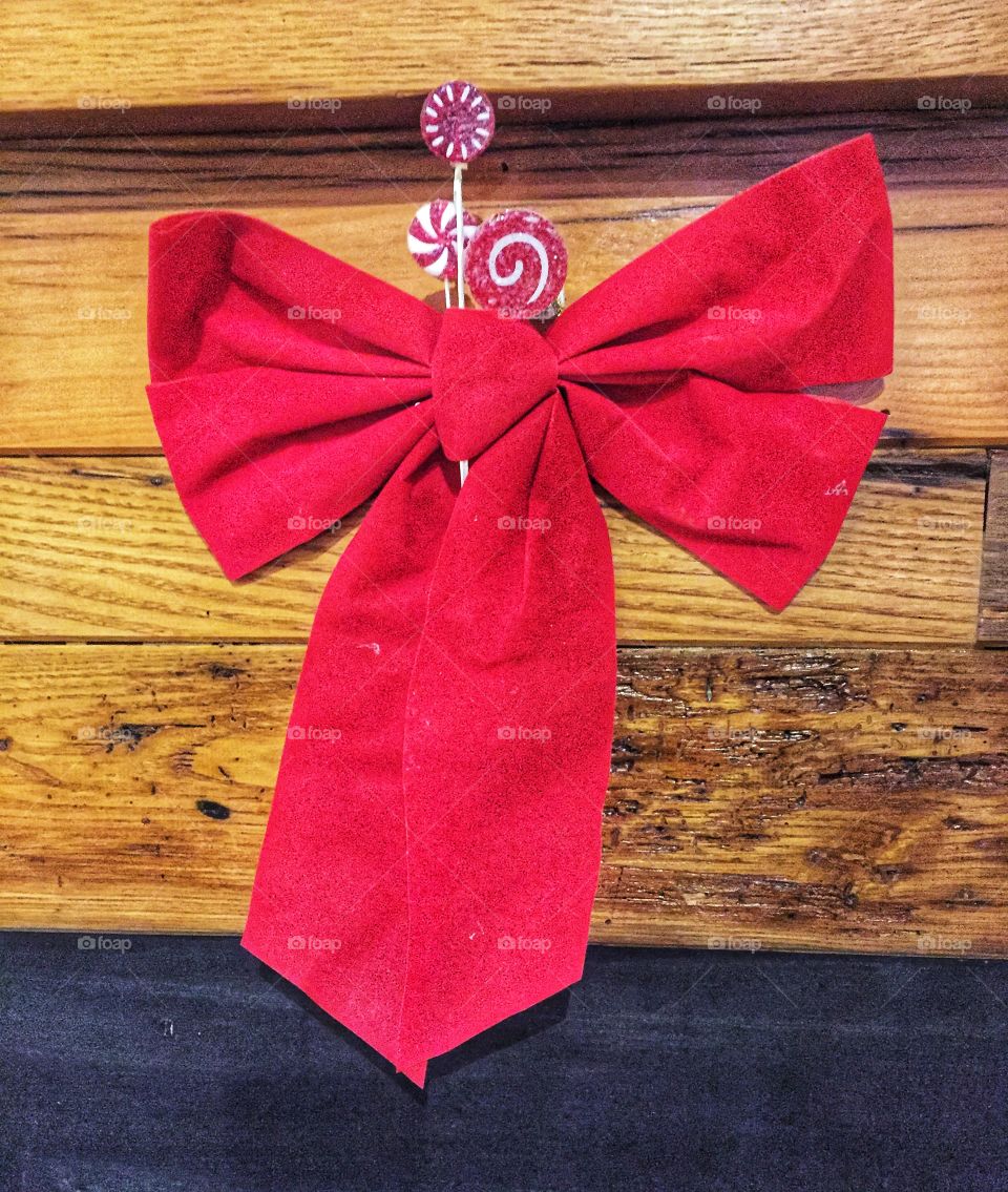 This red Christmas bow hangs on a wooden wall. Festive candy highlights its brilliant color.
