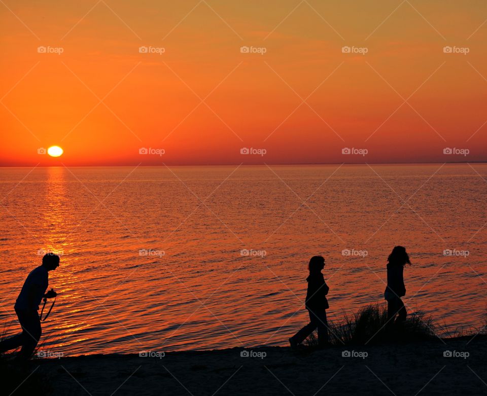 
A man and his children stroll along the sandy beach surrounded by an orange gold sunset which stretches far and wide