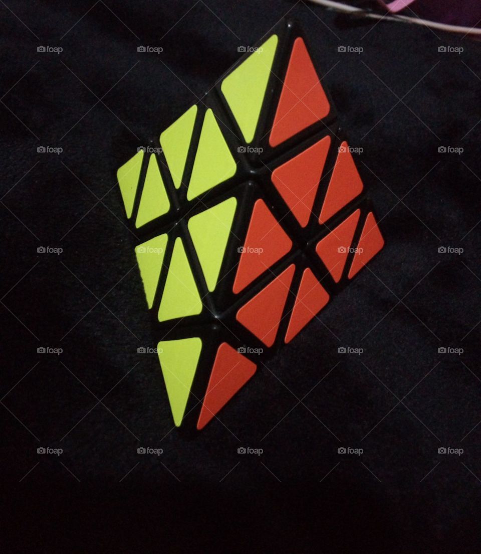 dos lados de un cubo Rubik pirámide. muestra triángulos de colores amarillo y naranja fosforescentes en un fondo negro