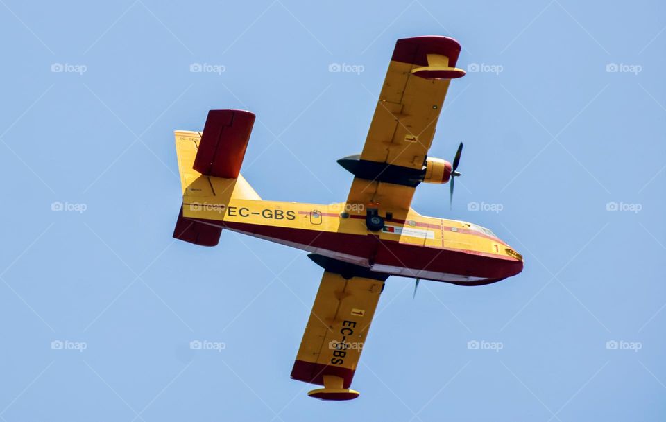 A yellow water plane flying by in the blue sky