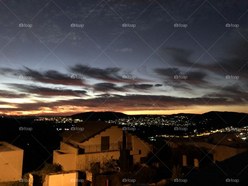 Blue and black sky with black clouds and yellow sunrise, and houses 