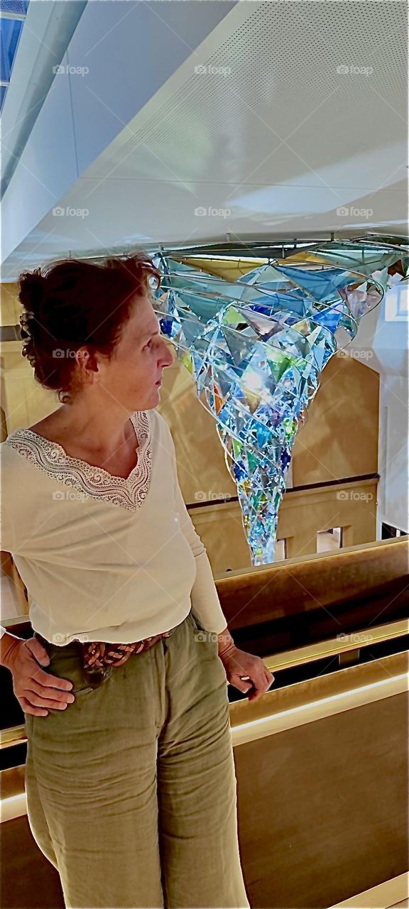 This lady is quite fascinated with the beautiful artwork, the paintings as well as the large pointy crystalline structure in blue with rainbow refractions on exhibit at the „Lenbachhaus“ in „Munich“, „Bavaria“, Germany. 2023. Hypnotic Productions