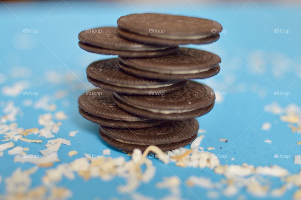 A stack of coconut Oreo thin cookies on a blue background with coconut shreds