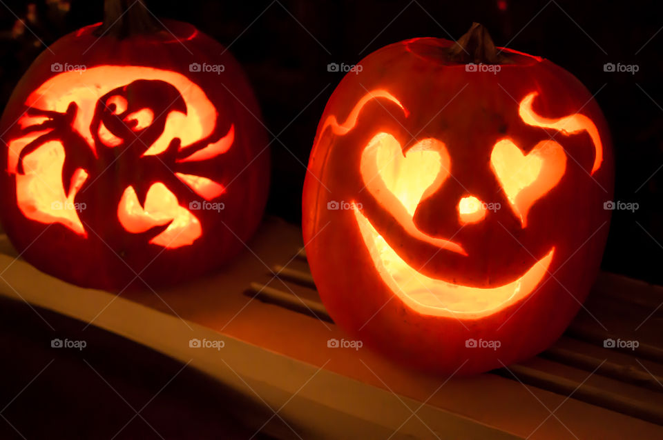 Cute heart shaped eyes and smiling face on Halloween jack o’lantern with pumpkin carved next to it on shelf at home with fun ghost with arms open to welcome trick or treaters or Halloween home party decoration centerpieces 