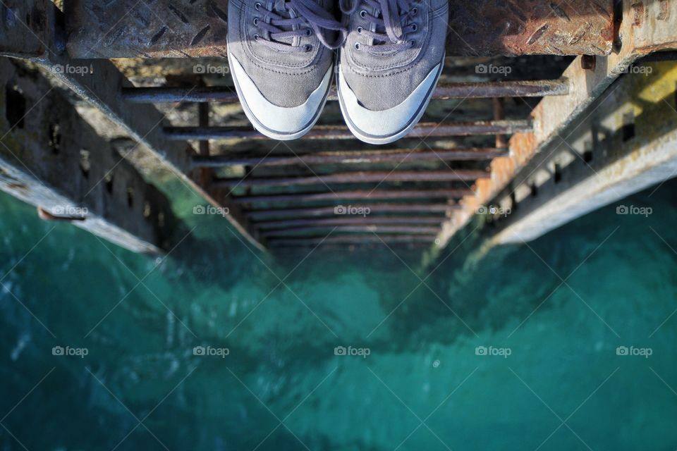 Looking down a rusty old ladder that leads to a green ocean with a pair of feet at the top ready to jump.