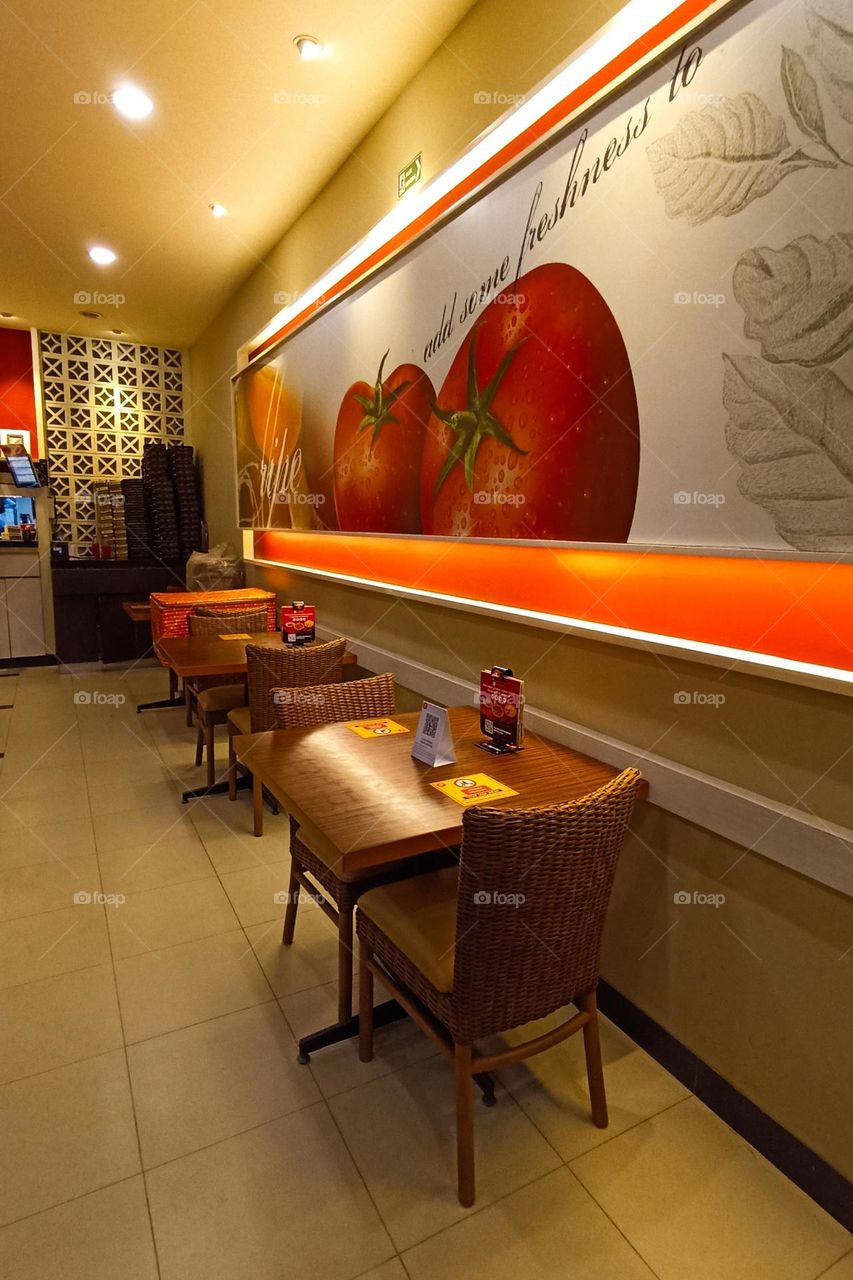 The interior of a restaurant with neatly arranged tables and chairs, large tomato themed walls, and warm lighting