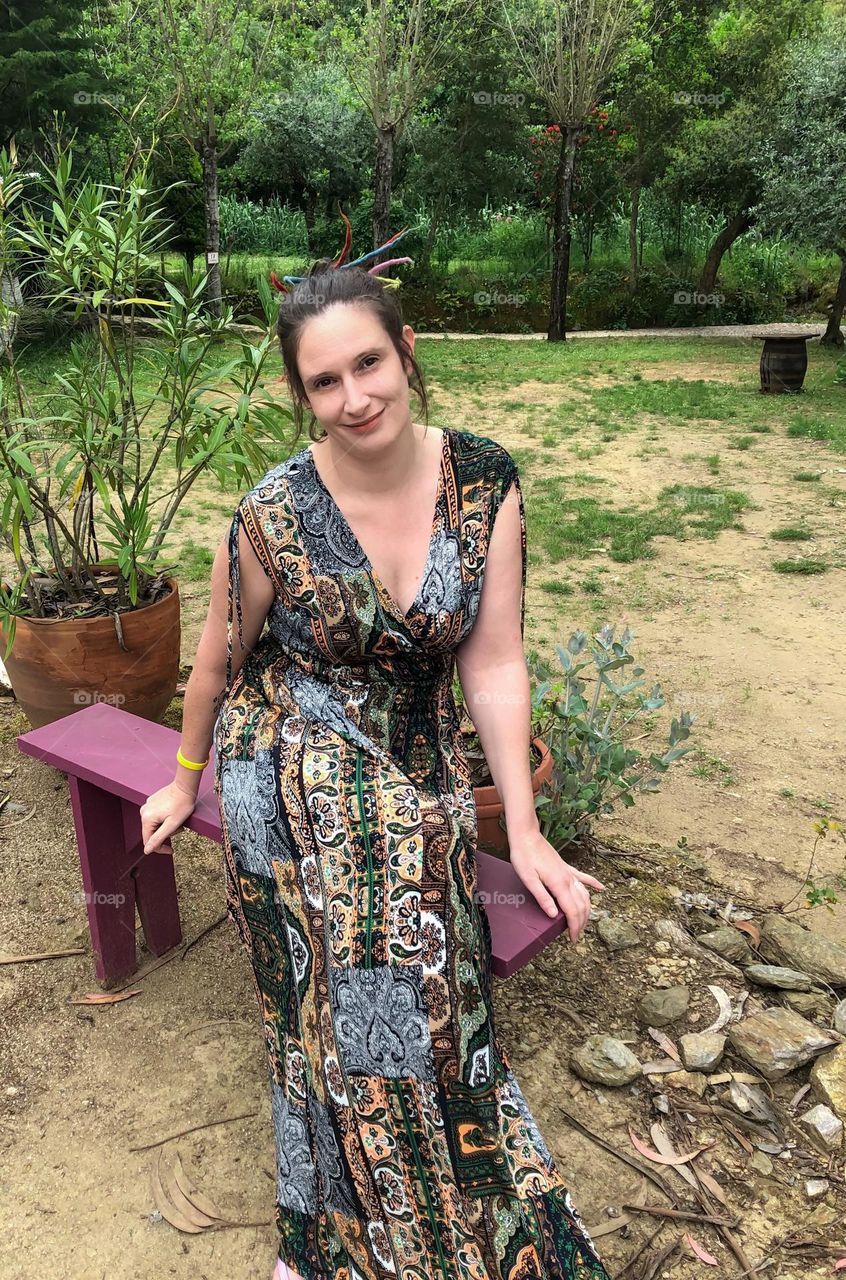 A woman sits on a beach wearing a summery maxi dress, in green surroundings 