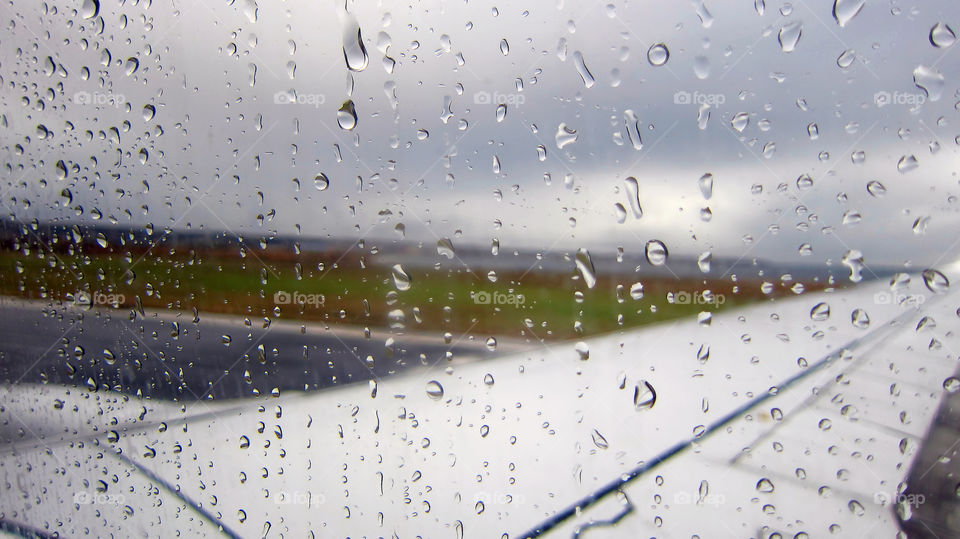 Raindrops on airplane window by the runway. A rainy day on an airport runway. Raindrops falling on the side glass window.