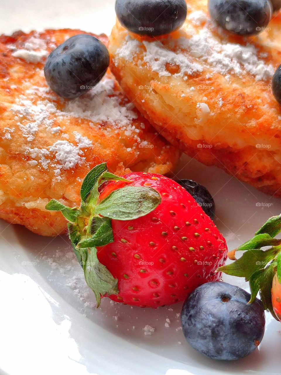 cheese pancake sprinkled with white powder. Berries of black blueberries and red strawberries lie on cheese pancake
